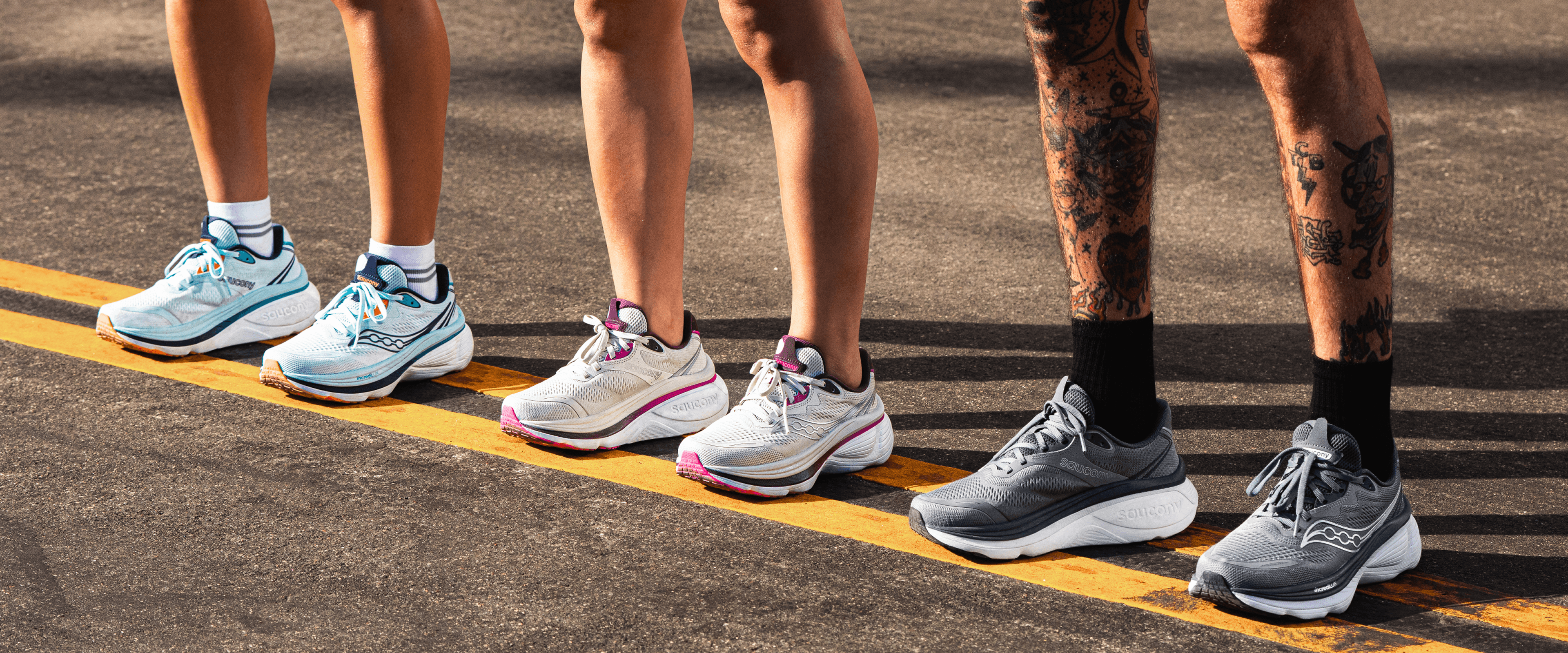 Three runners standing at a starting line wearing different colorways of Saucony running shoes.