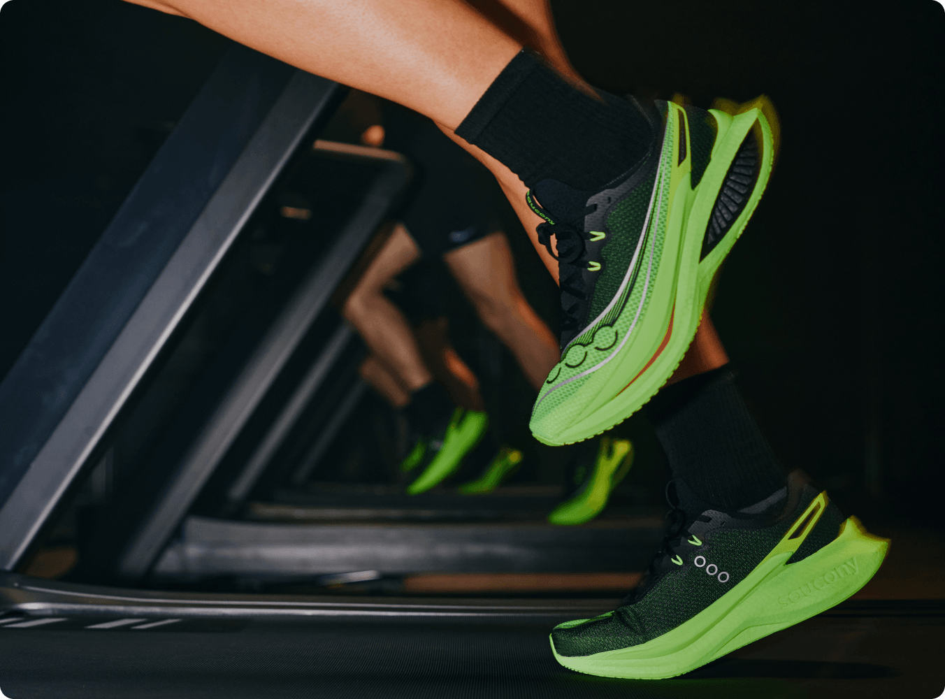 A runner wearing bright green Saucony shoes mid-stride on a treadmill.