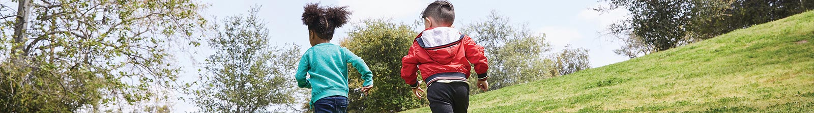 Girl and boy running up a hill full of green grass.